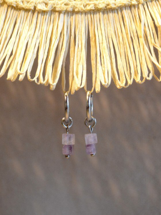 Aretes Belai Amatista, argollas de acero plateado con dije colgante de piedra amatista bicolor rectangular, apoyados sobre fibra de rafia y lino