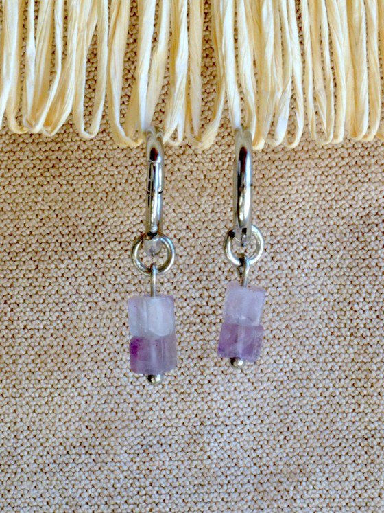 Aretes Belai Amatista, argollas de acero plateado con dije colgante de piedra amatista bicolor rectangular, apoyados sobre fibra de rafia y lino