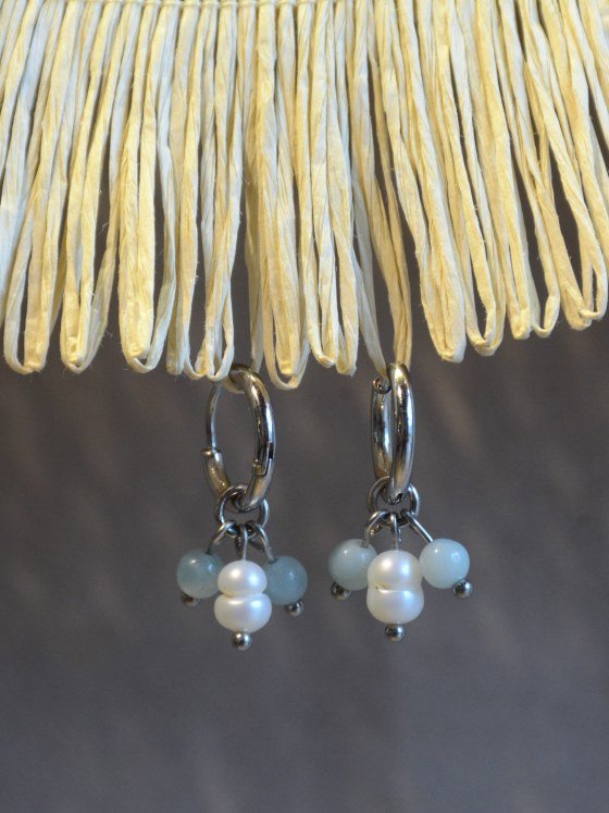 Aretes Belai Amazonita y Perla, argollas de acero plateado con dije colgante de cuentas de amazonita celeste y una perla blanca en el centro, apoyados sobre fibra de rafia y lino