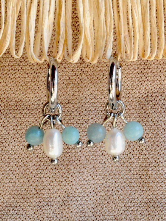 Aretes Belai Amazonita y Perla, argollas de acero plateado con dije colgante de cuentas de amazonita celeste y una perla blanca en el centro, apoyados sobre fibra de rafia y lino