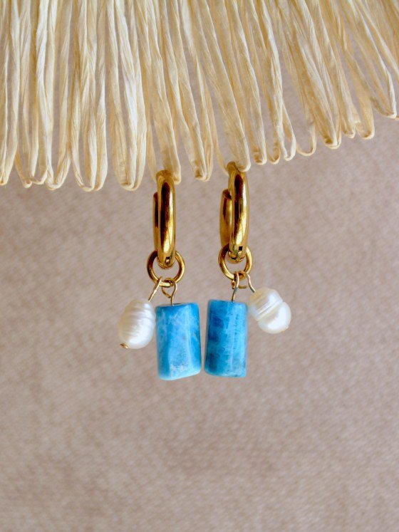 Aretes Belai Apatita y Perla, argollas de acero con racimo de tres cuentas en abanico: apatita azul, perla blanca y apatita azul, apoyados sobre fibra de rafia y lino