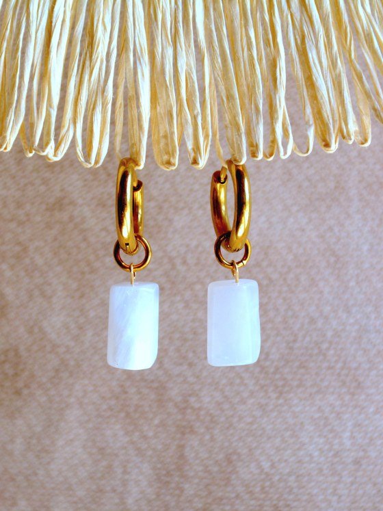 Aretes Belai Piedra Luna, argollas de acero con dije colgante de piedra luna blanca, apoyados sobre fibra de rafia y lino