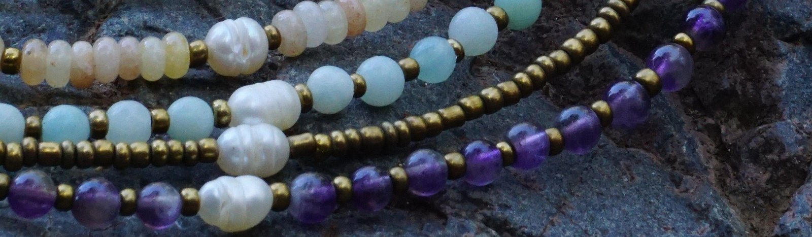 Collares Belai de piedras naturales — turquesa, amatista, perlas, cuarzo y amazonita — apoyados sobre una piedra