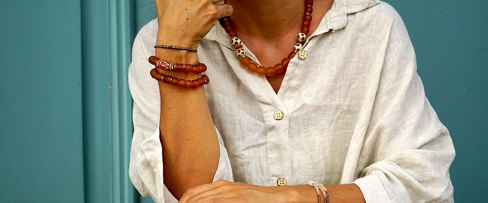 Mujer con collar y pulseras Belai de cuentas de vidrio reciclado en tonos ámbar, sobre una camisa de lino blanca