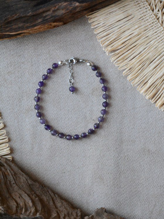 Pulsera Belai Amatista Plateada, cuentas de amatista con detalles plateados, apoyada sobre lino junto a madera y fibra natural