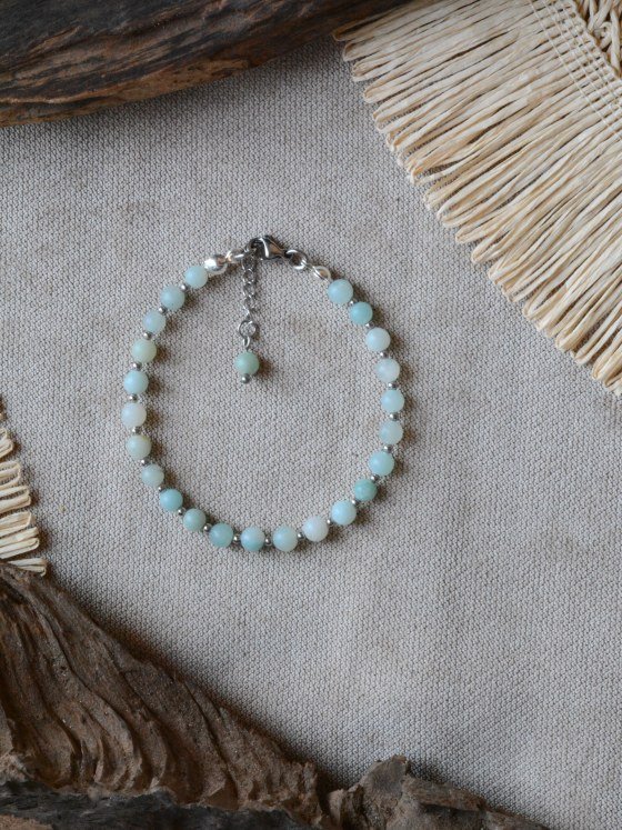 Pulsera Belai Amazonita Plateada, cuentas de amazonita verde-azulada con detalles plateados, apoyada sobre lino junto a madera y fibra natural