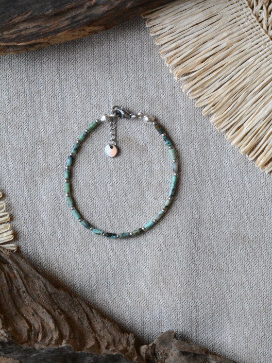 Pulsera Belai Turquesa Africana Fina Plateada, cuentas finas de turquesa africana con detalles plateados, apoyada sobre lino junto a madera y fibra natural